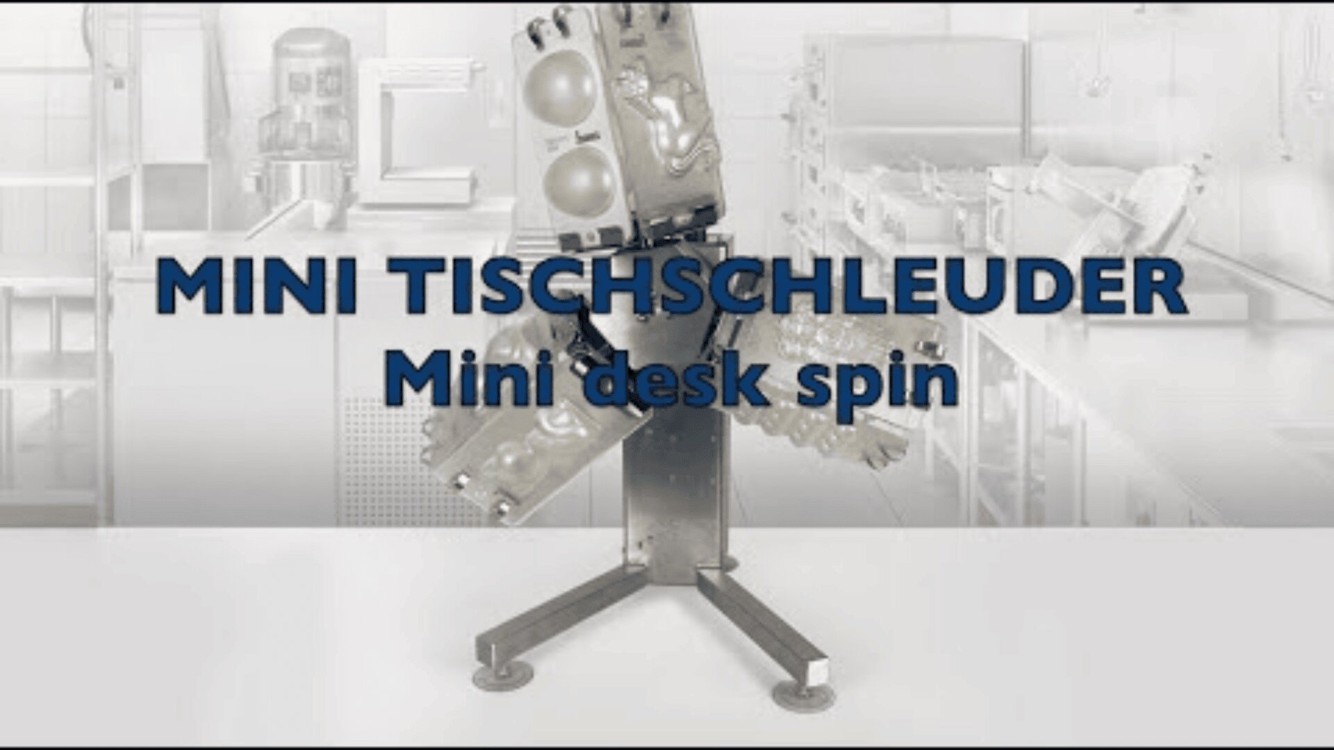 Eine kleine, metallene Laborzentrifuge mit Probenhaltern auf einem schrägen Ständer. Der fettgedruckte Text MINI TISCHSCHLEUDER und Mini desk spin steht vor einem unscharfen Laborhintergrund.