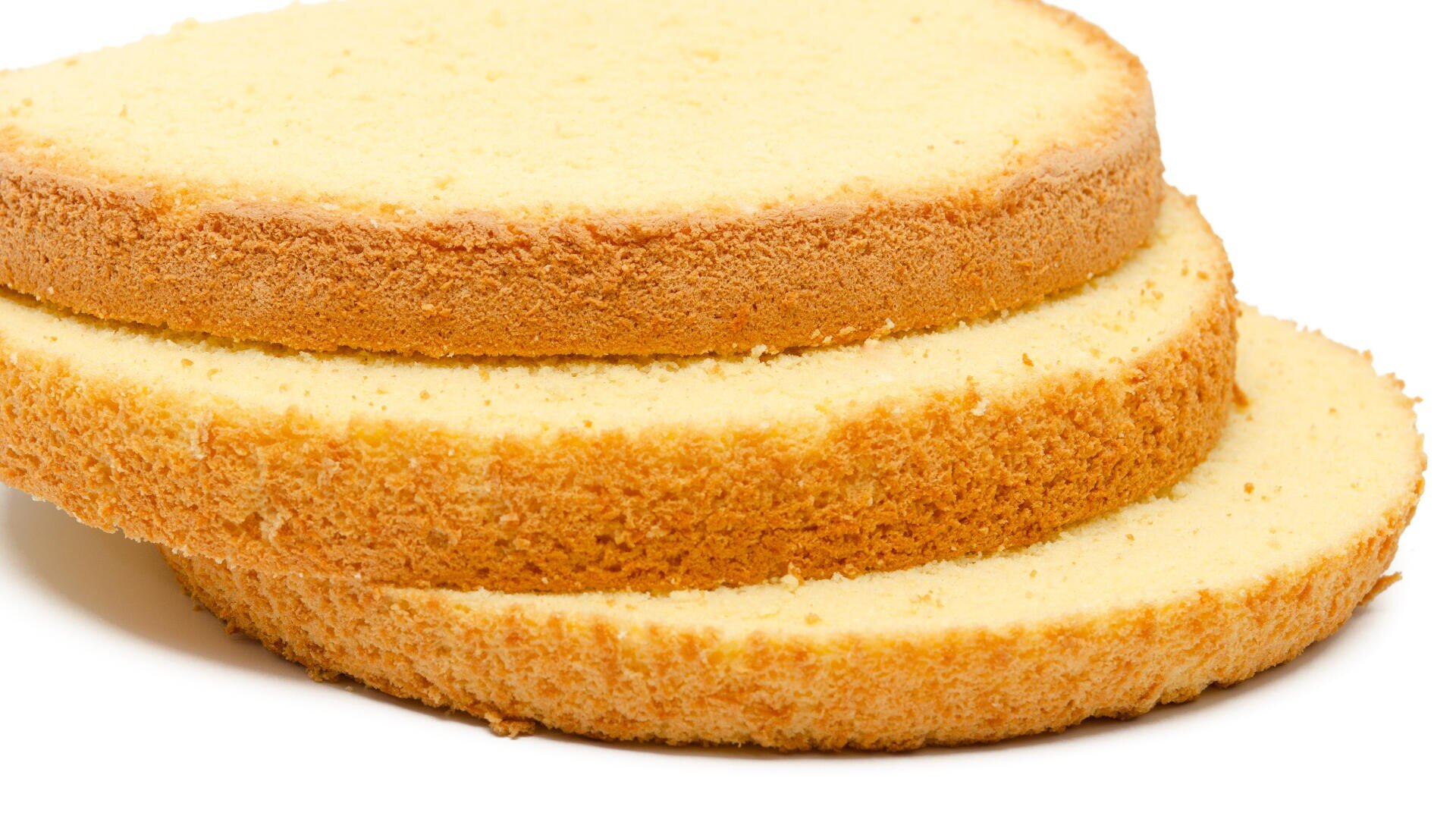Drei Scheiben einfacher gelber Biskuitkuchen, leicht übereinander gestapelt, mit weicher Textur und goldbraunen Rändern, isoliert auf einem weißen Hintergrund.
