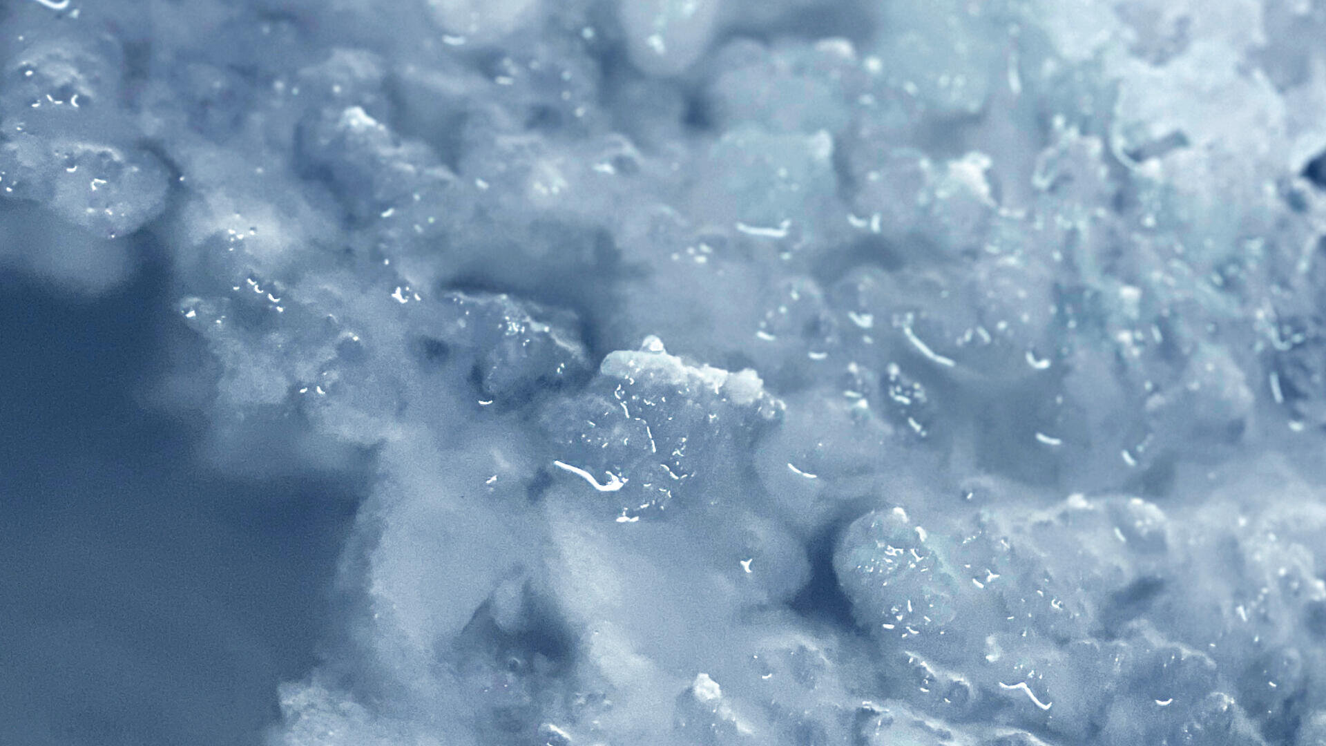 Nahaufnahme von zerstoßenem Eis mit unterschiedlich großen, glitzernden Eiskristallen, die eine kühle, strukturierte Oberfläche in Weiß- und Blautönen bilden.
