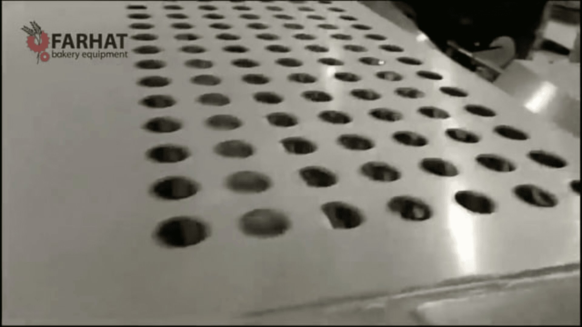 Ein Metall-Backblech mit mehreren runden Löchern, Teil einer industriellen Bäckereiausrüstung, ist in Schwarz-Weiß abgebildet. Das Logo von Farhat Bakery Equipment erscheint in der oberen linken Ecke.