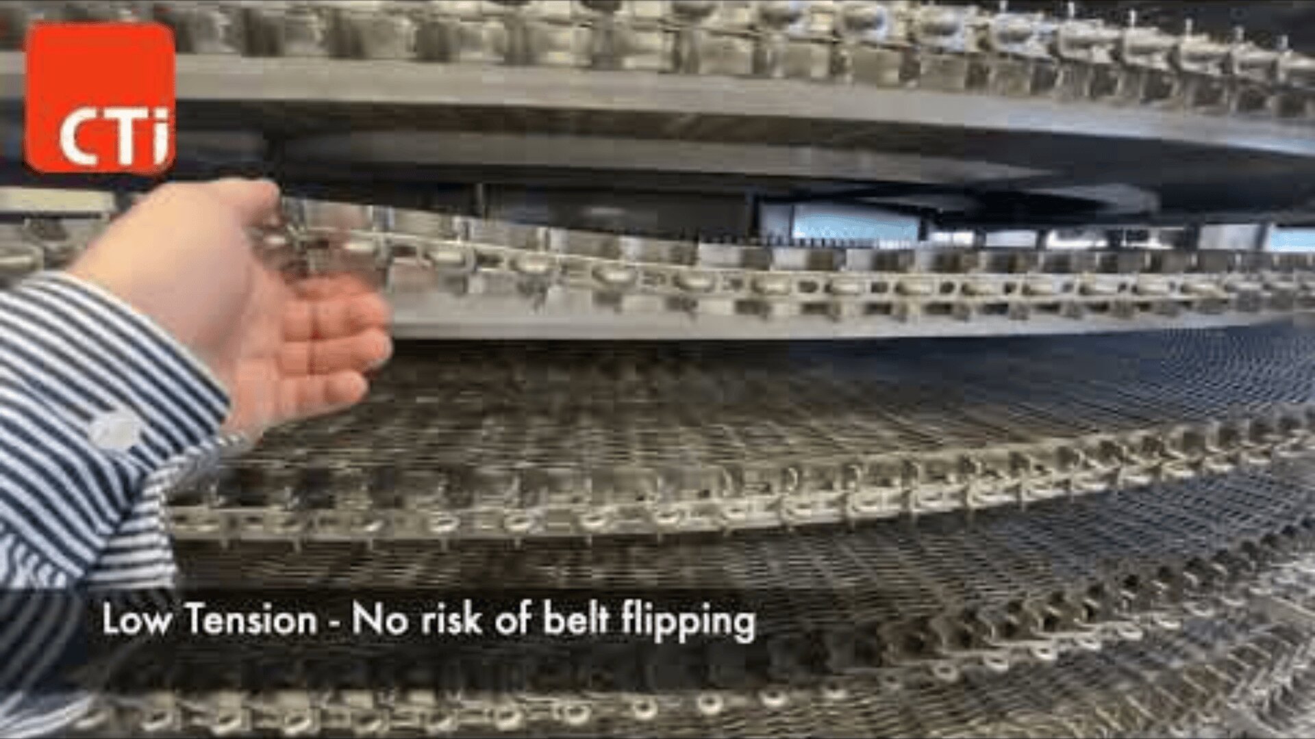 Eine Hand prüft ein Förderbandsystem aus Metall mit mehreren spiralförmigen Ebenen. Der Text lautet: „Niedrige Spannung – kein Risiko des Bandumkippens.“ In der oberen linken Ecke erscheint ein rotes CTi-Logo.