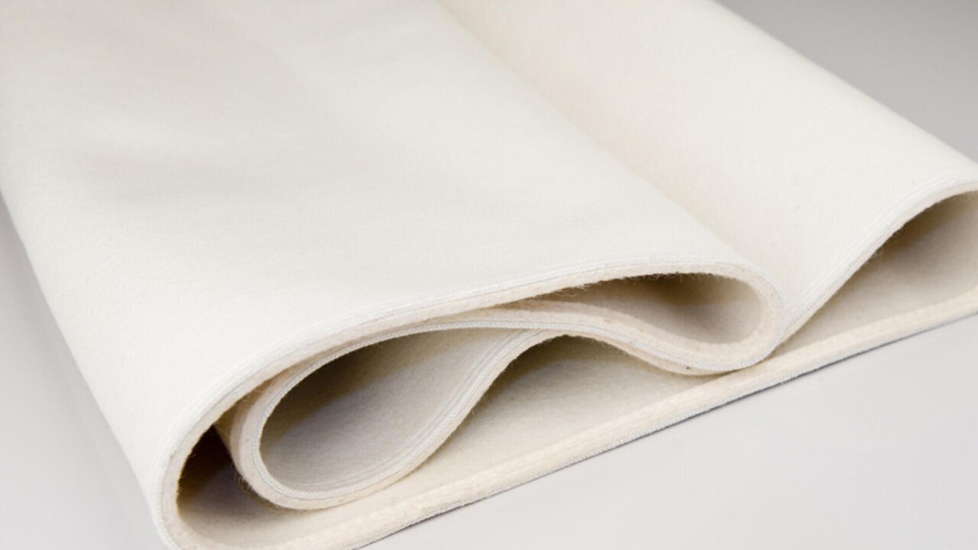 A close-up of a piece of off-white fabric neatly folded in layers on a smooth, light-colored surface. The fabric appears soft and thick, with a slightly textured finish.