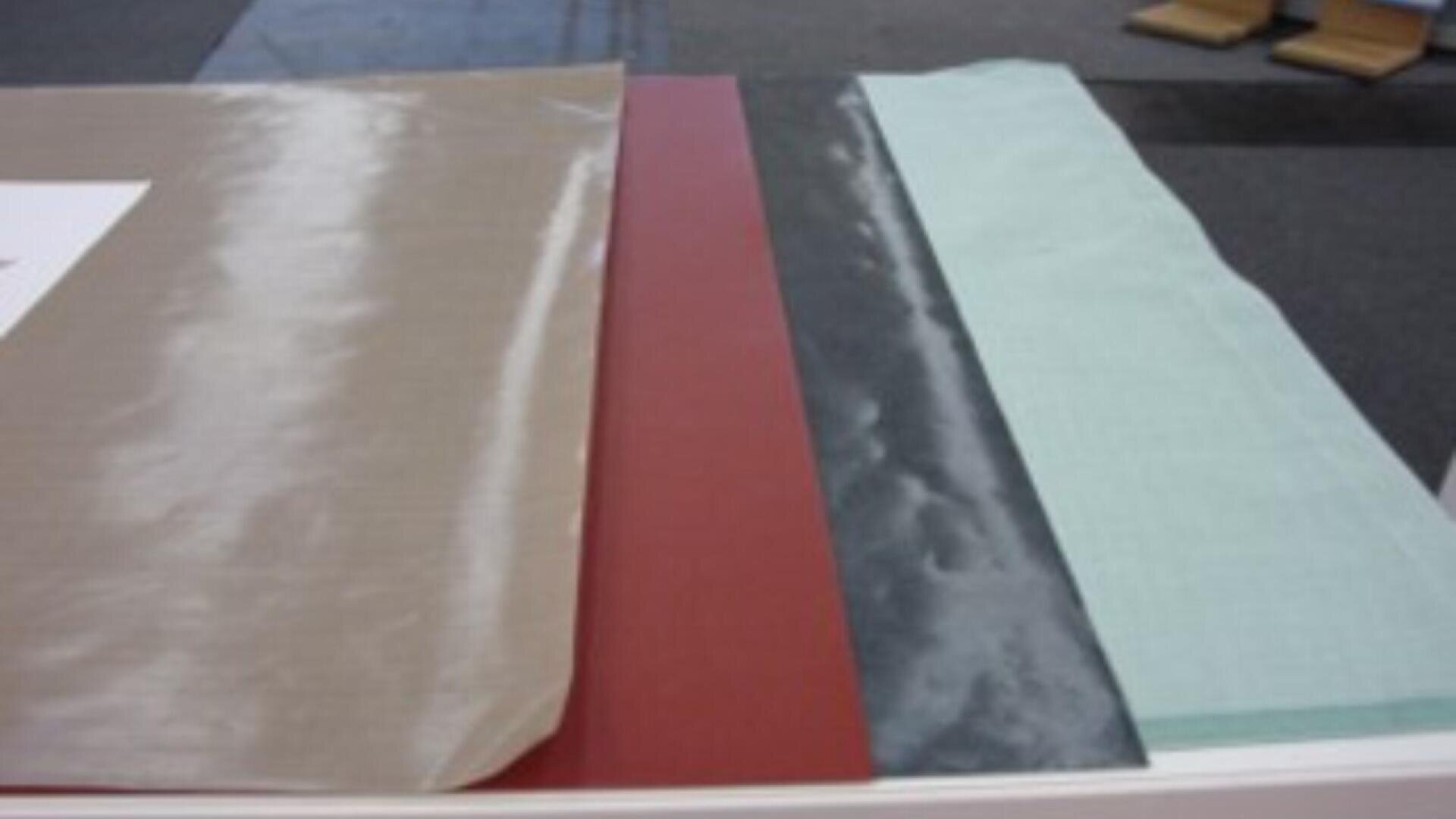 Four sheets of fabric or material in beige, red, dark gray, and light blue are laid out side by side on a white surface, possibly for display or comparison.