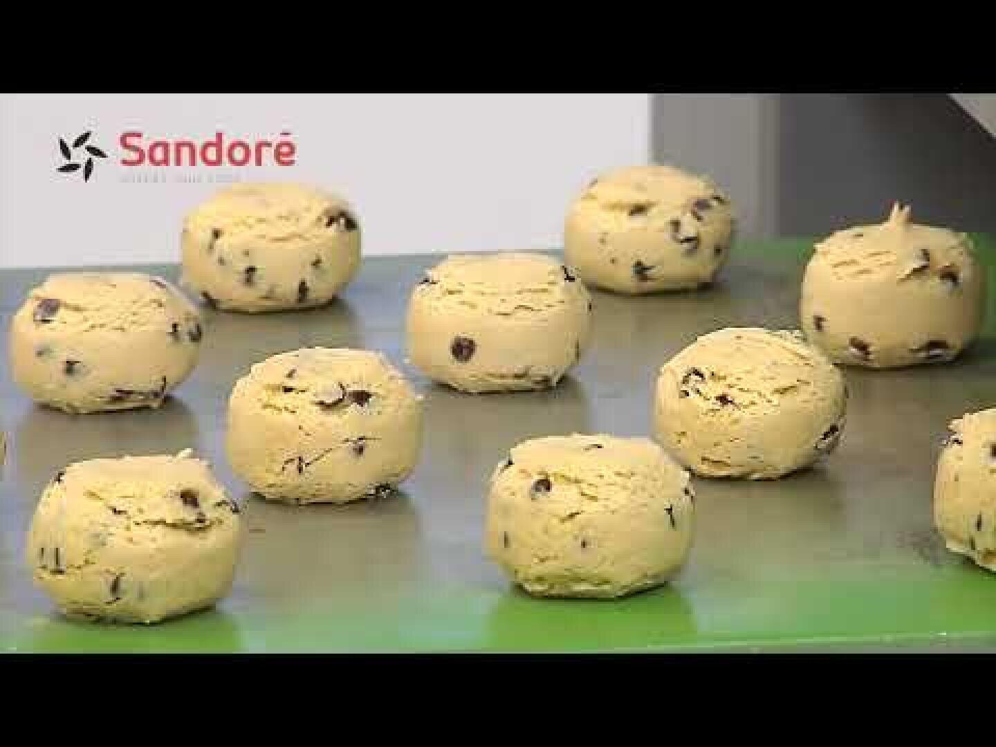 Several unbaked, round balls of chocolate chip cookie dough are arranged on a green tray. The Sandoré logo can be seen in the top left-hand corner of the picture.