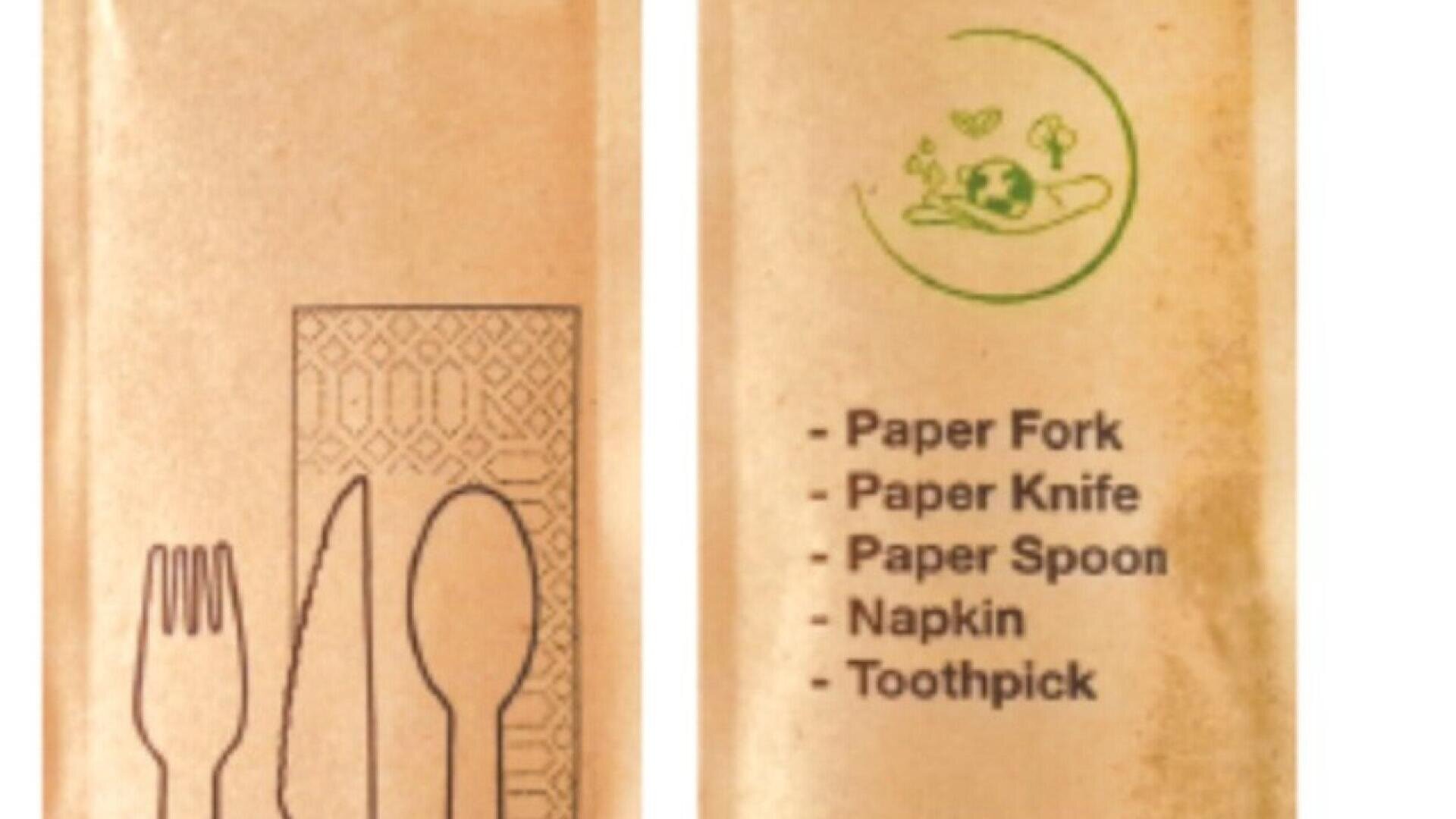 Zwei braune Papiertüten; eine zeigt schwarze Strichzeichnungen einer Gabel, eines Messers, eines Löffels und einer Serviette, die andere listet den Inhalt auf: Papiergabel, Papiermesser, Papierlöffel, Serviette, Zahnstocher mit einem grünen umweltfreundlichen Symbol darüber.