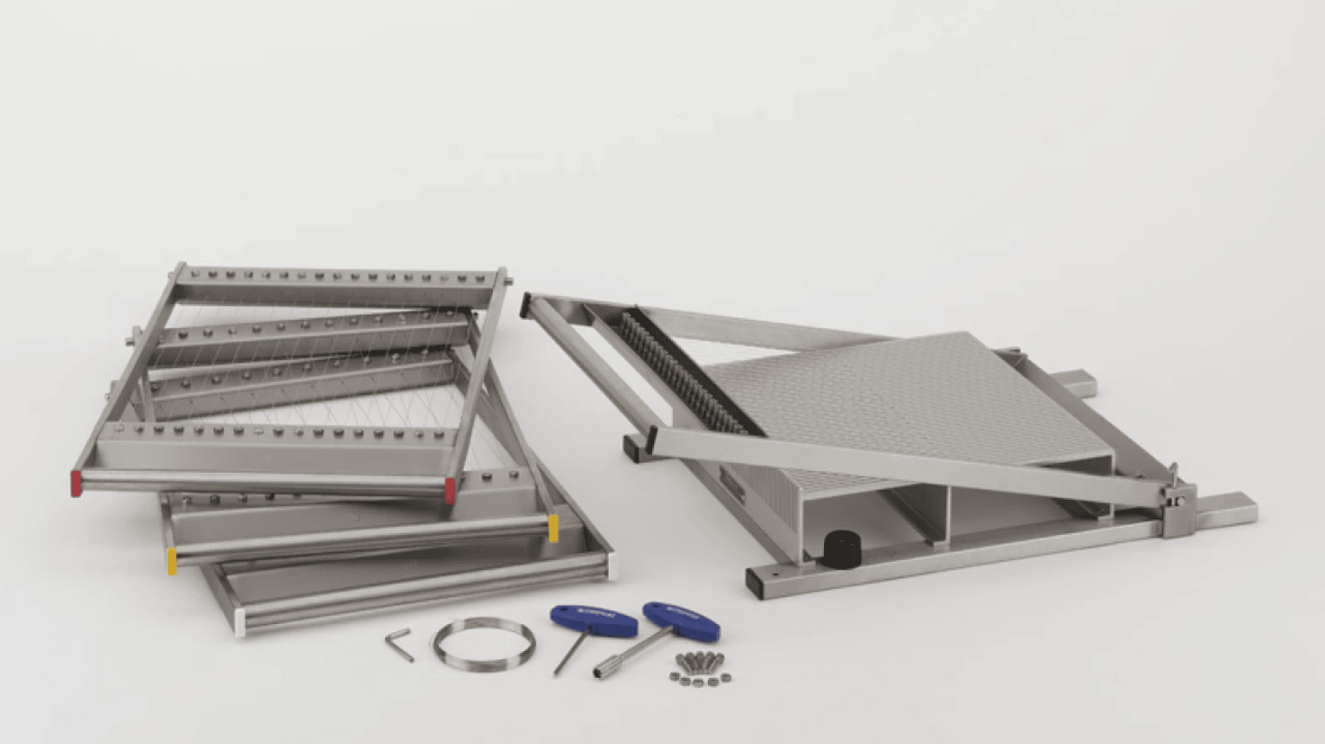 A metal assembly kit with several silver components, including frames, a textured platform, screws, two blue-handled tools, an L-shaped hex key, and small metal parts arranged on a white surface.