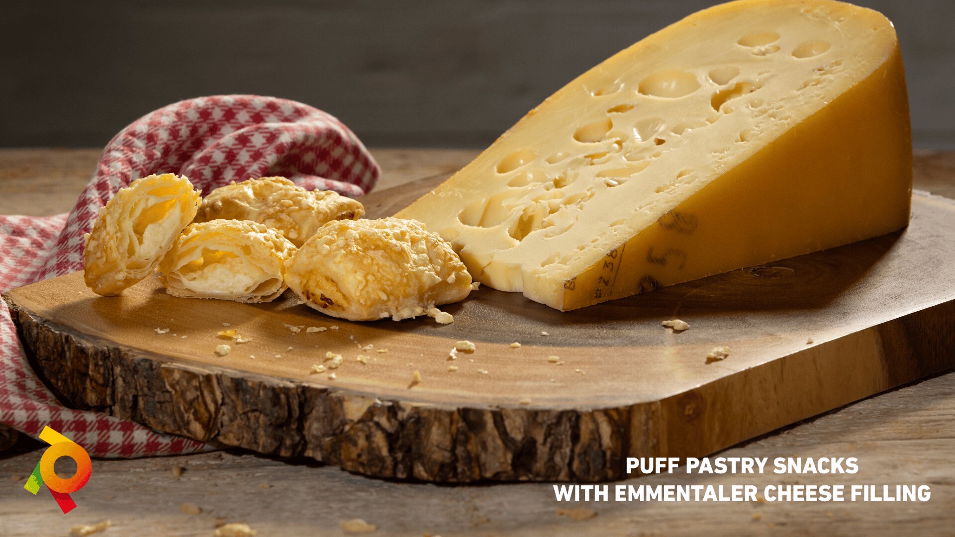 A large wedge of Emmentaler cheese and several golden puff pastry snacks sit on a wooden board, with a red-checkered cloth in the background. Text reads, Puff pastry snacks with Emmentaler cheese filling.