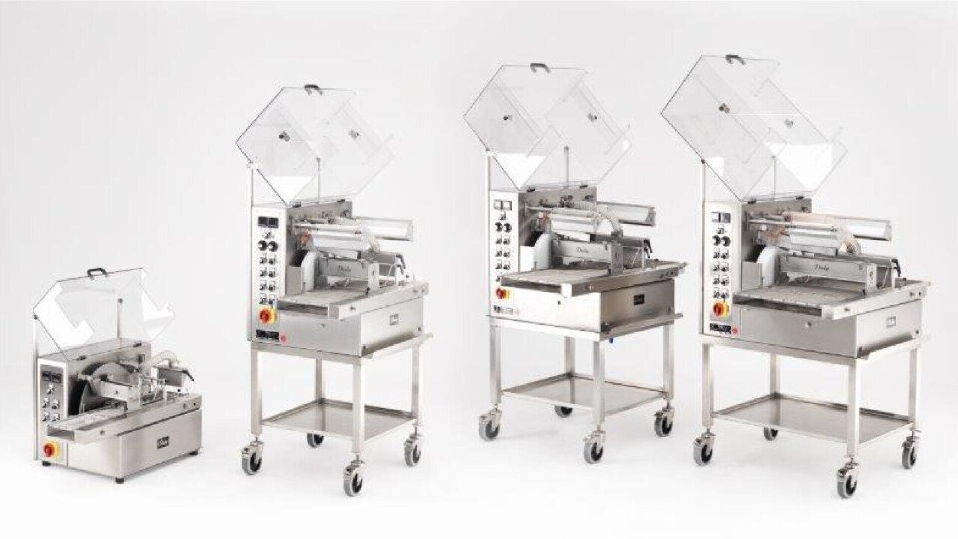Four industrial vacuum packaging machines of varying sizes are displayed in a row on white background; each machine has a transparent lid and control panel, with the three larger models mounted on wheeled stands.