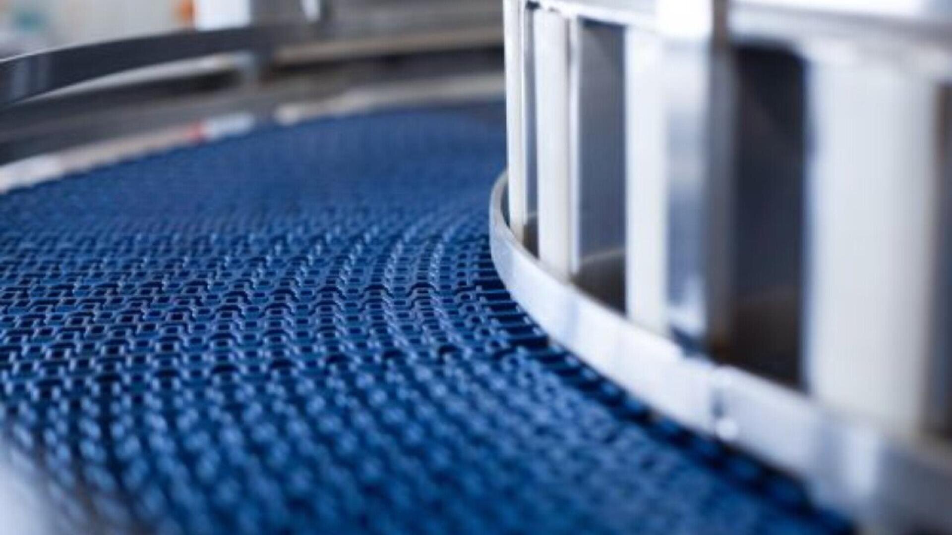 Nahaufnahme eines blauen, gebogenen Förderbands mit Metallrahmen, wahrscheinlich in einer Industrie- oder Fertigungsumgebung.