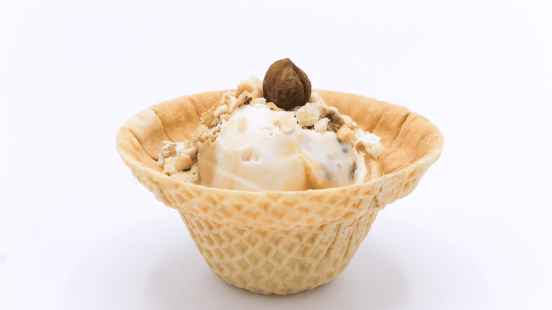 Eine mit einer Kugel Vanilleeis gefüllte Waffelschale mit gehackten Nüssen und einer ganzen Haselnuss, vor einem schlichten weißen Hintergrund.