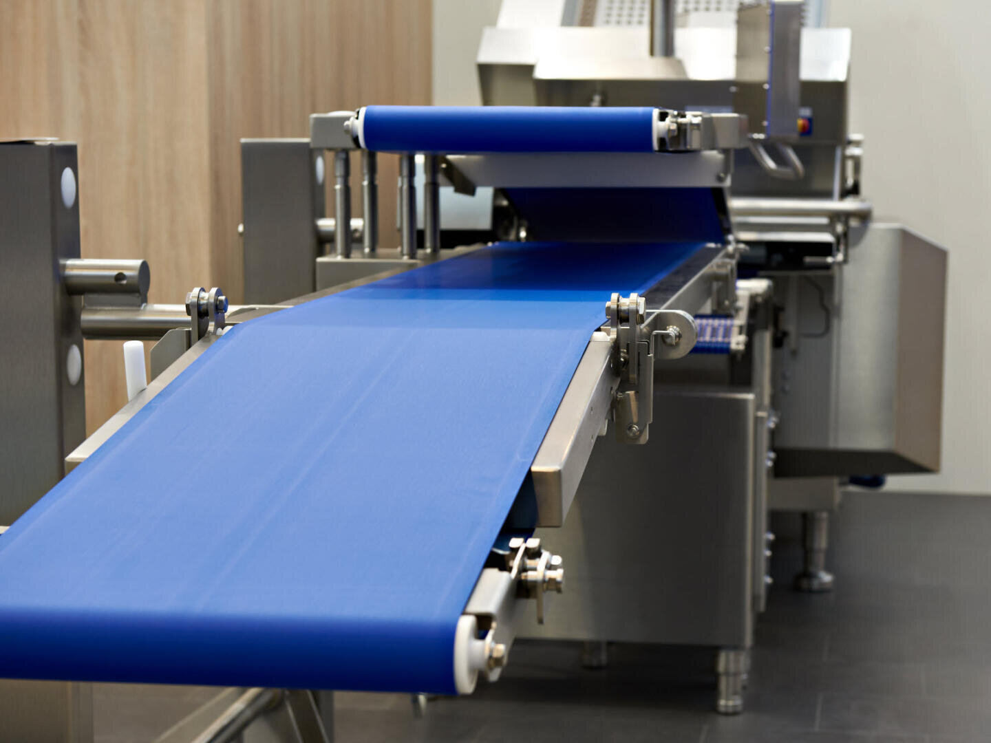 Nahaufnahme eines modernen industriellen Förderbands mit blauer Oberfläche, das Teil einer Lebensmittelverarbeitungsmaschine aus Edelstahl in einer sauberen Innenumgebung ist.