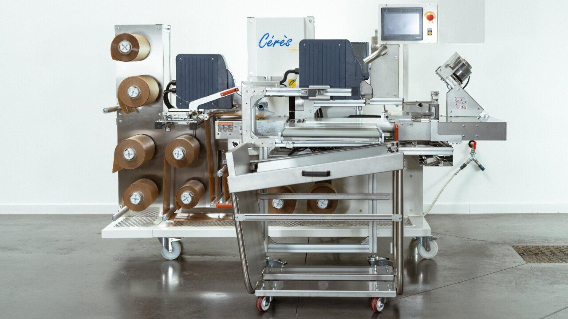 Eine kommerzielle Verpackungsmaschine mit mehreren Rollen braunen Papiers, Edelstahlkomponenten, einem Touchscreen-Bedienfeld und dem Etikett "Cérès" auf einem polierten Betonboden.