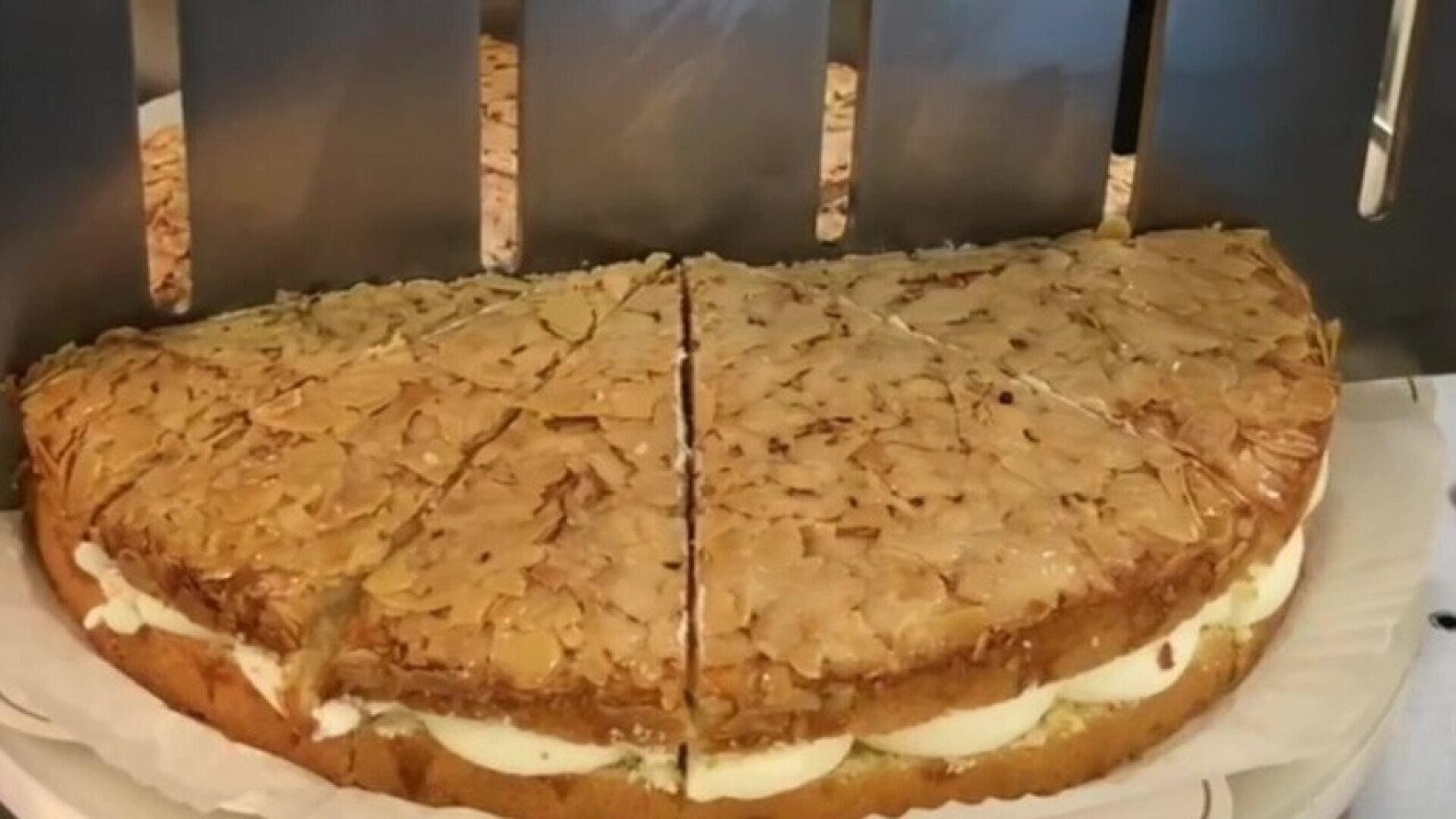 Ein mit Sahne gefüllter und in Scheiben geschnittener Mandelkuchen liegt auf einem Teller bereit zum Servieren. Der Kuchen hat einen goldenen, flockigen Mandelbelag und ist in gleichmäßige Portionen aufgeteilt.