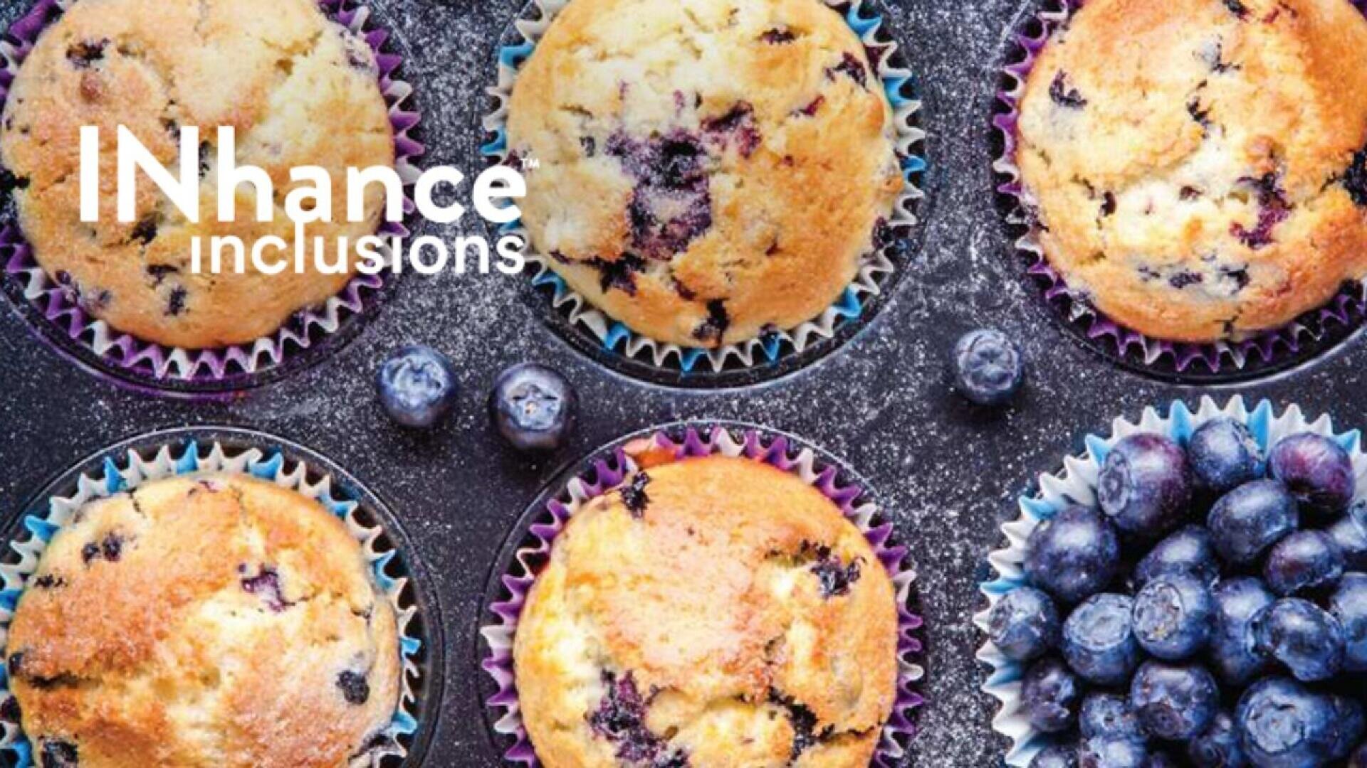 Sechs Blaubeermuffins in Papierförmchen sind auf einer dunklen Fläche mit verstreuten Blaubeeren und Puderzucker angeordnet. Der Text auf der linken Seite lautet "INhance Einschlüsse". Ein Haufen frischer Blaubeeren befindet sich unten rechts.
