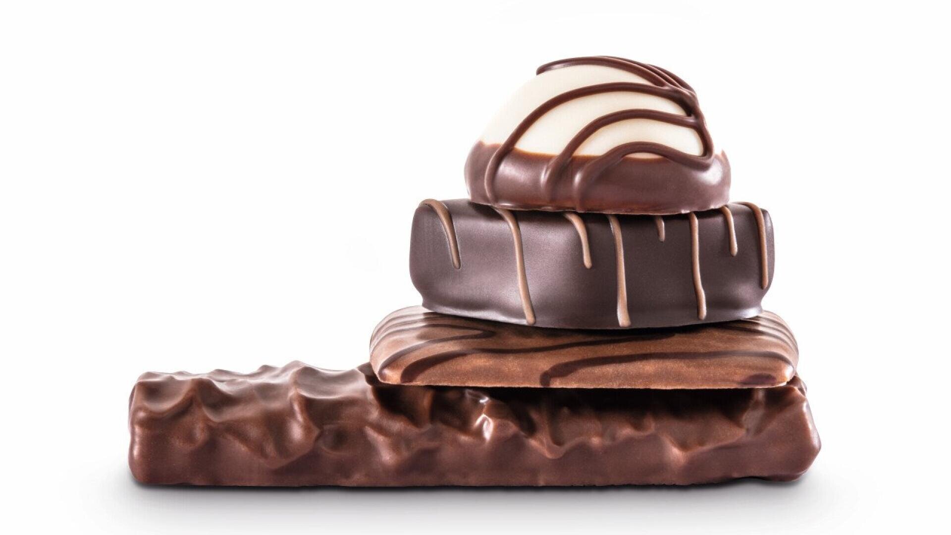 Three different shapes of chocolate candies stacked on top of a rectangular chocolate bar, all covered in glossy chocolate with decorative drizzles, on a white background.