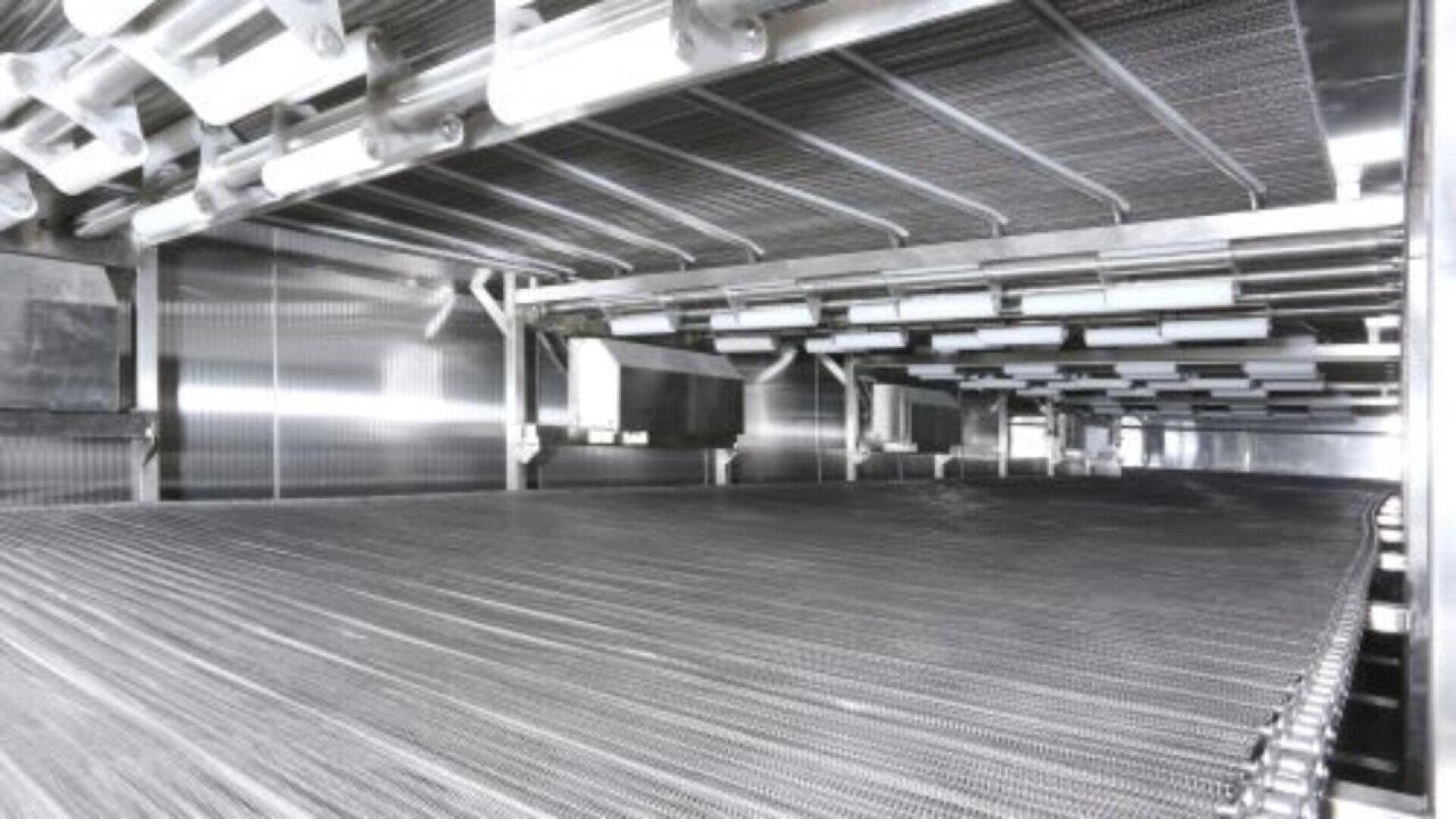 Nahaufnahme eines industriellen Förderbandsystems in einer Edelstahlverarbeitungsanlage. Zu sehen sind Metallrollen, Bänder und Überkopfkomponenten in einer sauberen, modernen Umgebung.