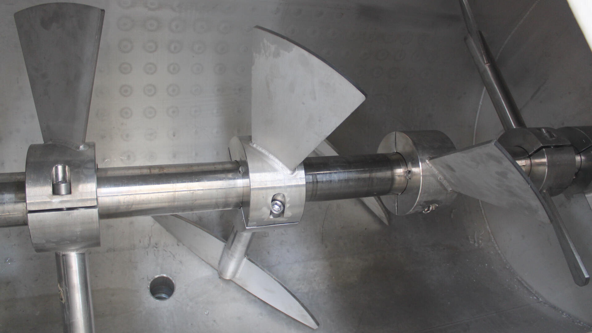 Nahaufnahme eines Industriemischers aus Edelstahl mit mehreren abgewinkelten Mischflügeln, die an einer rotierenden Welle in einem Metallbehälter befestigt sind.