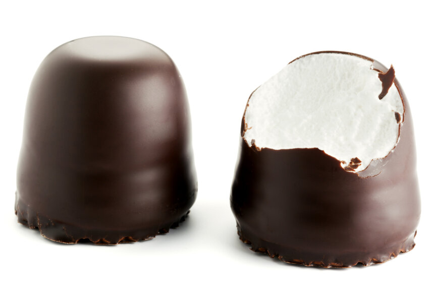 Zwei mit Schokolade überzogene Marshmallows sind vor einem weißen Hintergrund abgebildet; einer ist ganz, der andere ist angebissen, so dass die flauschige weiße Marshmallow-Füllung im Inneren sichtbar wird.